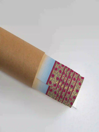 The Mewar wall art print partially unrolled from its kraft paper shipping tube, showing a blue-to-peach ombre panel and a magenta floral border.
