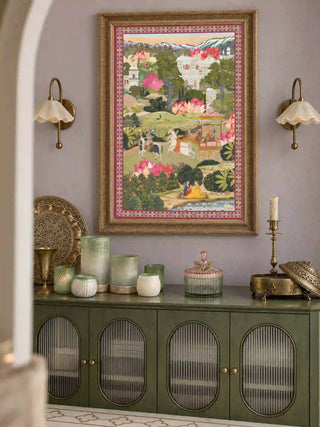 The Mewar wall art print in a carved gold frame above a sage green sideboard styled with brass vessels and glass votives, between two brass sconces.