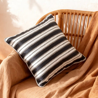Midnight Linea monochrome cushion styled on a rattan chair with a warm throw.