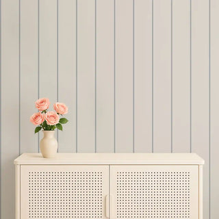 Minimal gray & beige vertical stripe wallpaper styled behind a cream console with a vase of pink roses, giving the space a refined, calming feel.