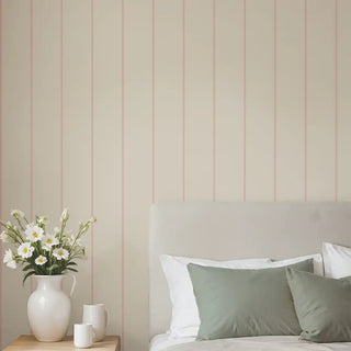 Minimal pink and beige striped wallpaper behind a soft neutral bed with green cushions, creating a calm and cozy bedroom look.