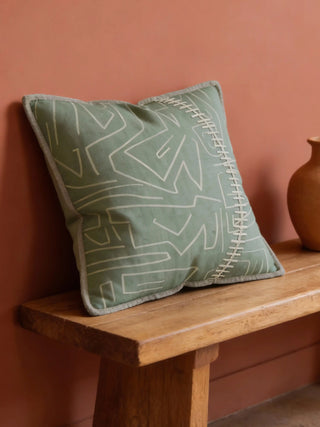 A luxury mint abstract cushion cover featuring sage green tones and ivory whipstitch details on a rustic wooden bench.