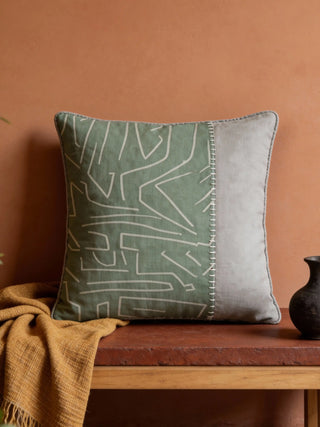 A luxury Mint Block cushion cover featuring sage green abstract patterns and a grey panel on a dark wooden bench.
