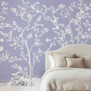 A lavender Chinoiserie wallpaper featuring delicate white floral blossoms and branches, styled behind a bed with soft neutral bedding.