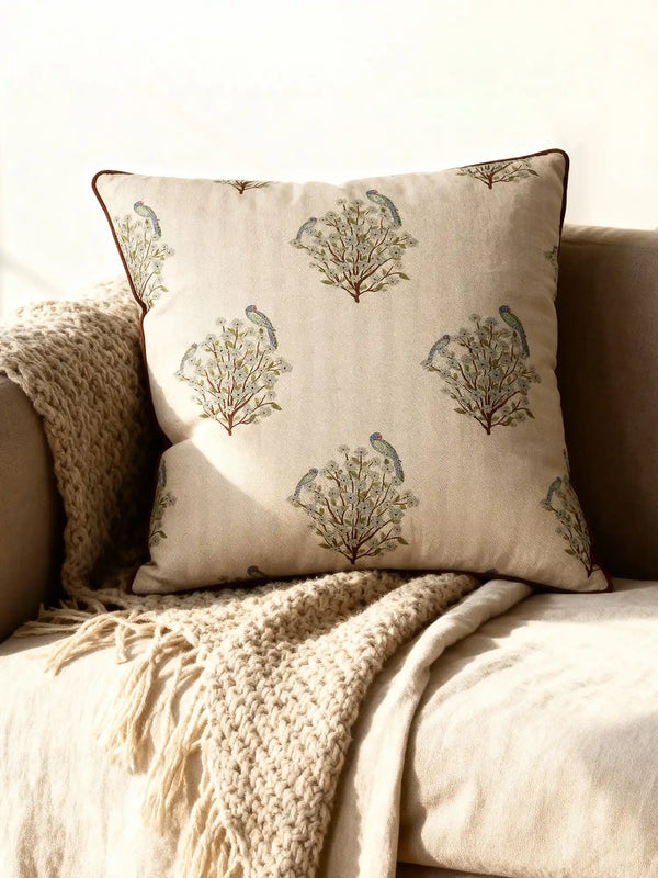A luxury Mithoo cushion cover in natural linen featuring embroidered parakeets on flowering trees with a brown piped border.