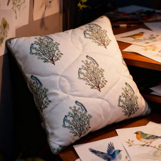 Artistic lifestyle shot of the parrot-motif cushion in a creative, warm-lit workspace.