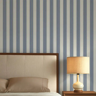 Bedroom wall featuring Modern Blue & Grey Wide Stripe Wallpaper Roll, styled with alternating wide blue and soft grey vertical stripes behind a beige upholstered bed and warm bedside lamp.