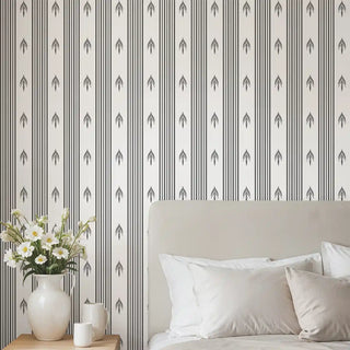 Bedroom wall decorated with Modern Charcoal & White Arrow Stripe Wallpaper Roll, featuring vertical charcoal stripes with repeating arrow motifs, styled behind a beige upholstered bed and fresh white linens.