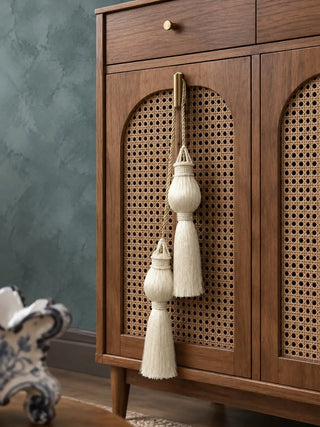 Moonlit ivory curtain tieback with two beaded tassels hanging from a dark wooden bedpost