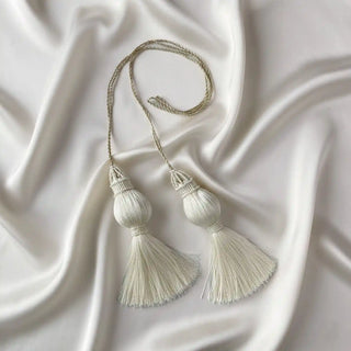 Flat lay of the Moonlit Tassel showing the two ornate tassels with beadwork and the silvery braided cord on a satin background.