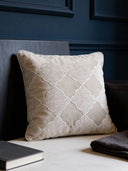 A luxury beige velvet cushion with white Moroccan lattice embroidery styled against a dark blue paneled wall