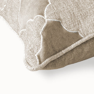 Close-up of the beige cushion corner showing the white embroidered quatrefoil pattern.