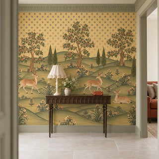 The Mriga Vatika wallpaper in an entryway behind a dark-wood console with a fringed lamp and white flowers, deer grazing beneath the trees view-foyer