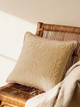 A luxury clay-colored quilted velvet cushion with pink piping styled on a woven rattan armchair.