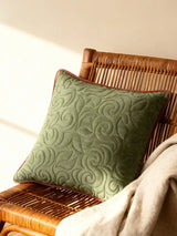 A luxury Mughal Bel cushion cover in sage green velvet with architectural quilted vine patterns resting on a rattan chair.
