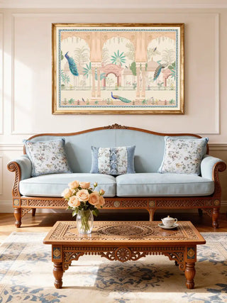 A sophisticated living room featuring the Mughal Garden mural with peacocks displayed above a light blue tufted sofa and carved wooden table.