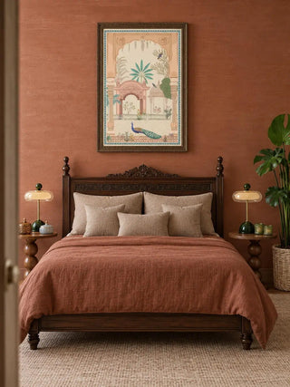 Mughal Garden portrait wall art in a dark carved frame above a carved four-poster bed with terracotta linen, beige cushions, green-based lamps and a monstera plant, on a terracotta wall.