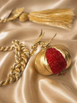 A detailed macro close-up of the Nar tieback highlighting the metallic gold pomegranate surface and glistening red glass seed beads.