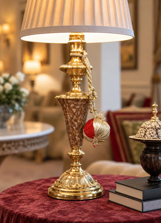 The Nar charm in Gold & Red, view-lampbase hanging from a brass table lamp.