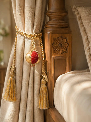 The Nar hand-beaded pomegranate curtain tieback holding back drapes on a luxury carved wooden four-poster canopy bed frame.