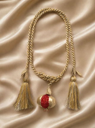 A high-resolution flatlay shot of the Nar luxury pomegranate curtain tieback showing its braided gold ropes and ruby-red beadwork on satin.