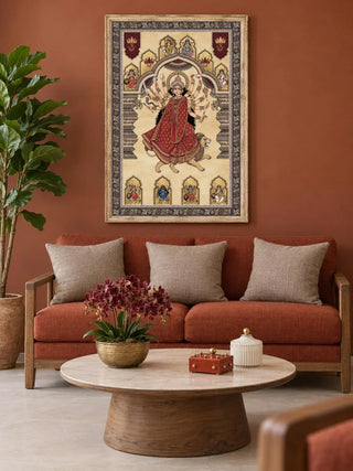 Framed Navadurga Virajitam wall art in a pale wood frame above a terracotta sofa with oatmeal cushions and a round marble coffee table in a living room