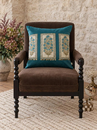 The Nayab velvet cushion cover in Teal on a dark upholstered armchair, styled in a maximalist stone-walled room.
