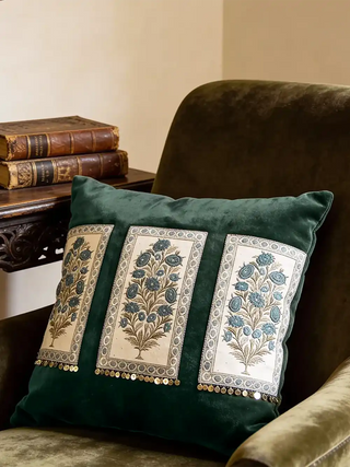 The Nayab dark green botanical cushion styled on a velvet armchair next to vintage leather-bound books.