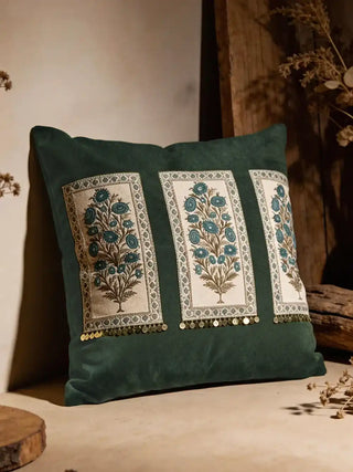 A studio shot of the Nayab olive green velvet cushion showing three embroidered botanical panels and gold coin fringe.