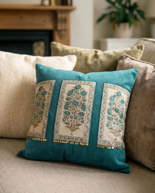 A lifestyle view of the Nayab teal botanical cushion in a warm living room setting with a fireplace.