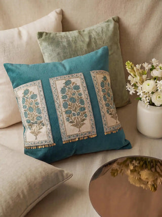The Nayab teal velvet cushion styled on a beige linen sofa with white flowers and a silver tray.
