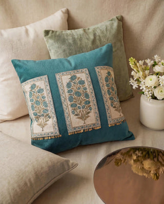 A lifestyle shot of the Nayab Teal Velvet cushion styled on a beige sofa with fresh white flowers and a reflective tray.