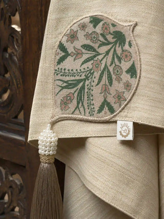 A detailed close-up view highlighting the hand-appliquéd green Mughal flower booti, seed pearls, and silk tassel of the Nazneen throw.