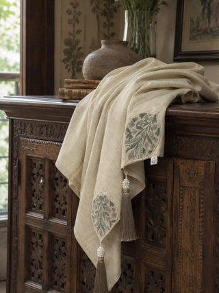 The Nazneen luxury hand-embroidered linen table throw elegantly draped over a vintage carved dark wood credenza cabinet.