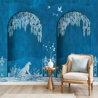 Decorative wall mural with white floral arches and a sitting figure on a blue background, featuring a chair and table.