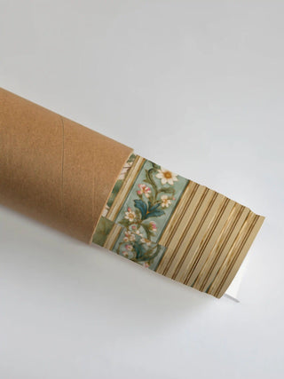The edge of the Nirvana Bloom wall art rolled in a brown kraft tube, showing the sage floral border and the pale gold band.