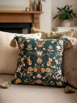 A lifestyle view of the nool-e-gul green embroidered cushion being placed on a neutral sofa.