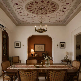 Noor Mahal ceiling mural in parchment and crimson overhead in a heritage Indian dining room with walnut dining table, cane-back chairs, terracotta arched alcove with brass accessories, white walls, and a brass ring chandelier