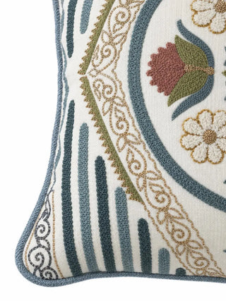 Close-up of the Noorani cushion cover corner showing teal stripes, a gold scrollwork band with green zigzag edge, a red bloom and blue piping