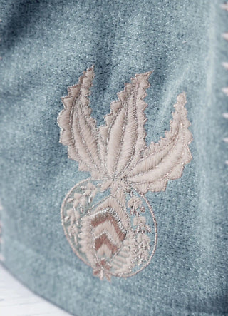 The Noush tea cosy in Dusty Blue, view-detail of the embroidered palmette-and-medallion emblem.