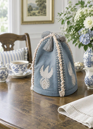 The Noush tea cosy in Dusty Blue, view-diningtable beside blue-and-white china and hydrangeas.