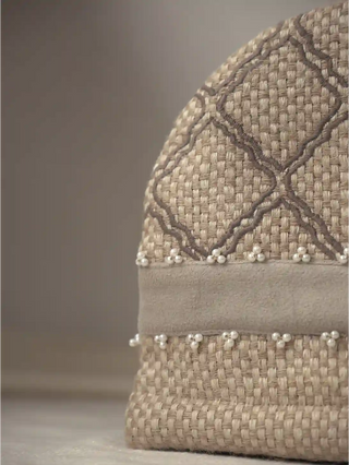 A high-resolution close-up view of the Oat Pearl tea cosy showcasing its basket-weave fabric, corded lattice embroidery, velvet band, and pearls.