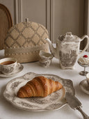 Oat Pearl tea cosy with pearl-beaded trim styled beside a vintage teapot and croissant on a breakfast table