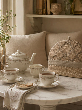 Oat Pearl tea cosy displayed on a marble table alongside a vintage floral teapot and teacups