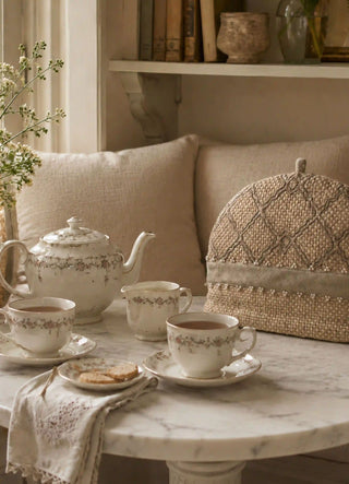 Oat Pearl tea cosy beside a floral porcelain tea set on a marble-topped table