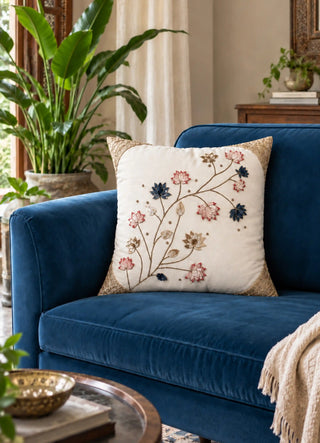 Padma Katha ivory cushion cover with hand-embroidered lotus branch on a navy velvet sofa beside a potted plant and carved wood console in a living room