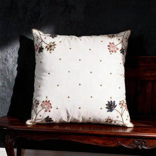 The Padma Leela ivory cushion styled on a dark mahogany bench, showcasing how the gold embroidery catches the light.