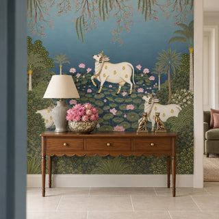 Padma Sarovar wallpaper behind a walnut console table with a scalloped apron, a grey ribbed lamp, a silver bowl of pink roses and two brass big-cat figurines.