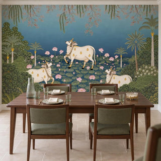 Padma Sarovar wallpaper behind a dark wood dining table with four olive-green upholstered chairs, set with floral plates, gold cutlery and a ribbed glass carafe.