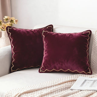 Two maroon velvet scallop cushions decorating a white sofa in a bright room.